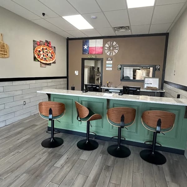 Jonuzi's Pizza interior with a green counter, bar stools, and a Texas flag on the wall.