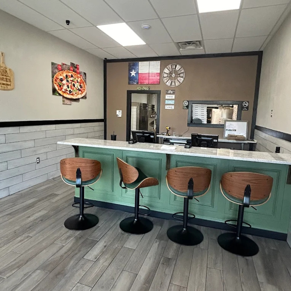 Jonuzi's Pizza interior with a green counter, bar stools, and a Texas flag on the wall.