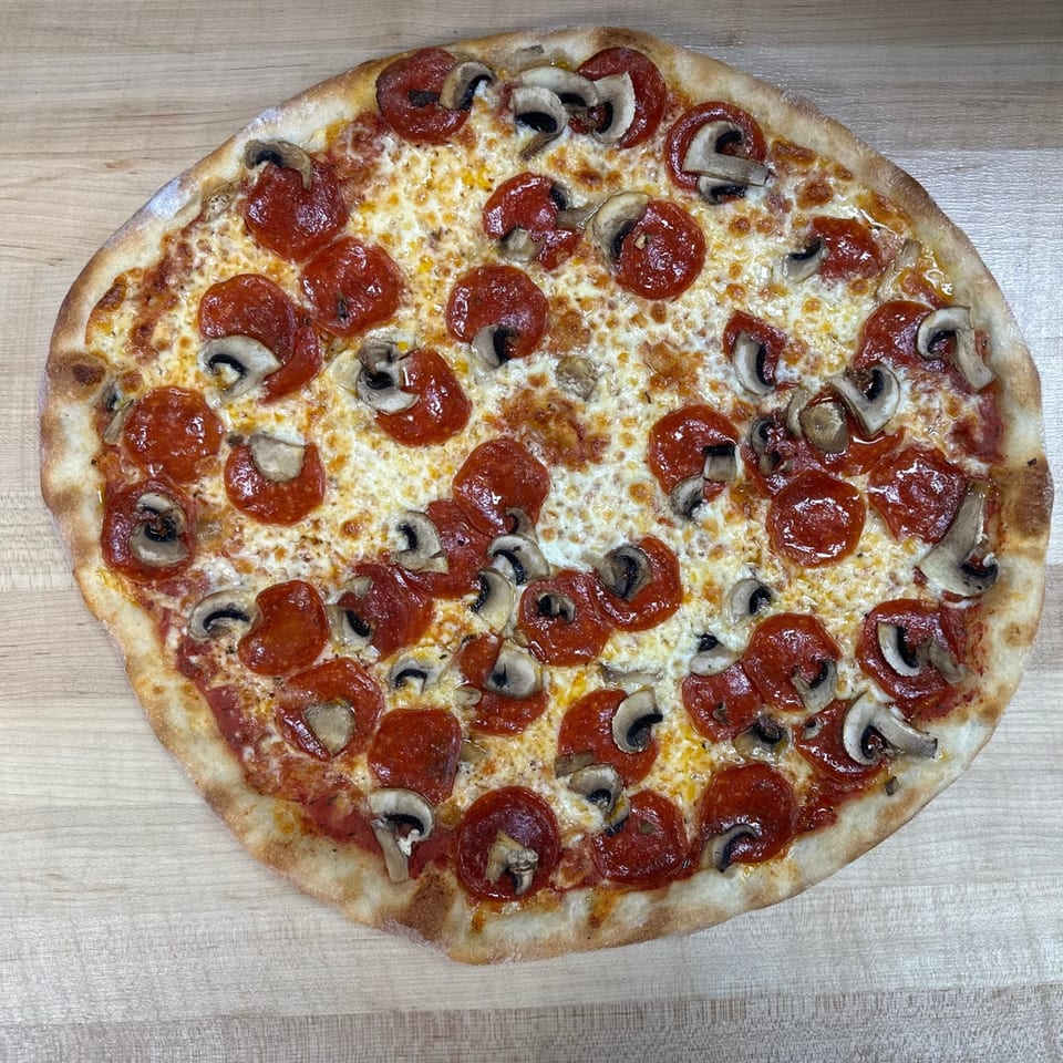 A whole Jonuzi's pepperoni and mushroom pizza with melted cheese on a wooden surface.