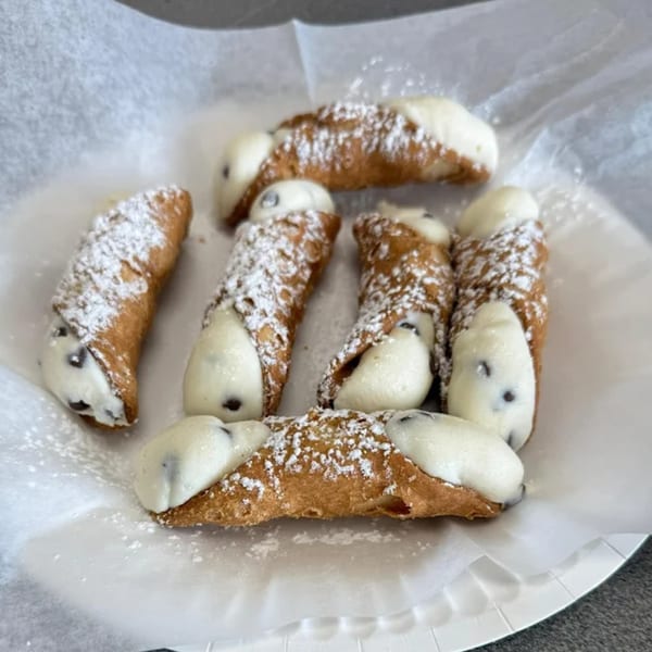 Seven Jonuzi's Pizza cannolis, filled with cream and chocolate chips, dusted with powdered sugar.