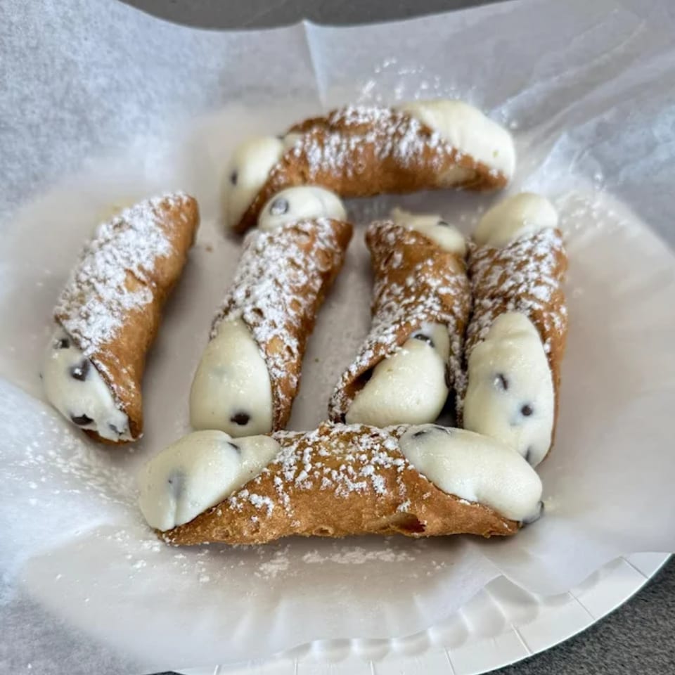 Seven Jonuzi's Pizza cannolis, filled with cream and chocolate chips, dusted with powdered sugar.