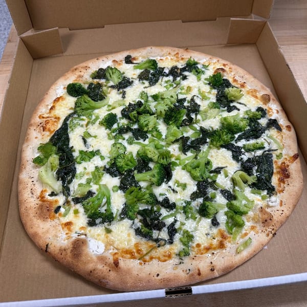 Jonuzi’s Pizza white pizza with broccoli and spinach in a cardboard box.