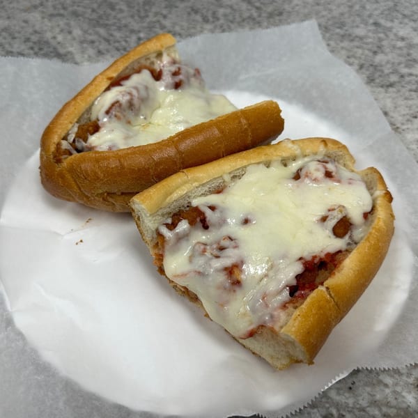 Two halves of a meatball sub sandwich with melted cheese and marinara sauce on a white plate.