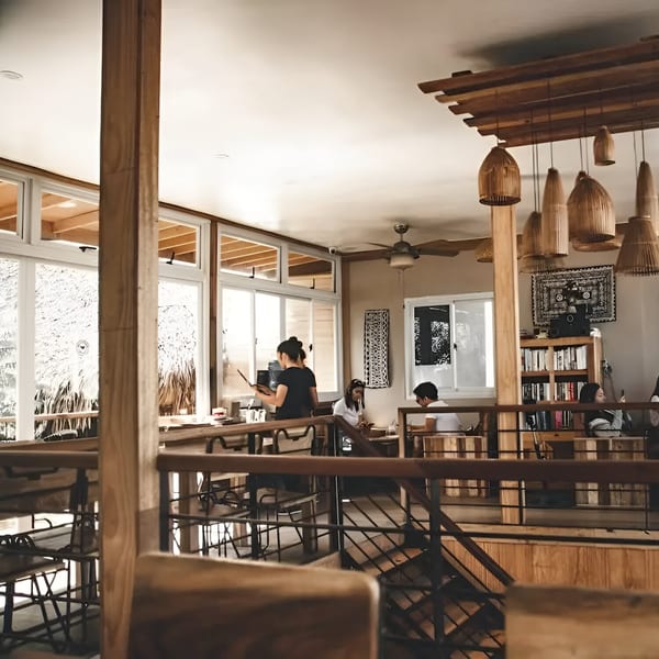 A bright, multi-level restaurant interior with wooden beams, bamboo light fixtures, and patrons dining.