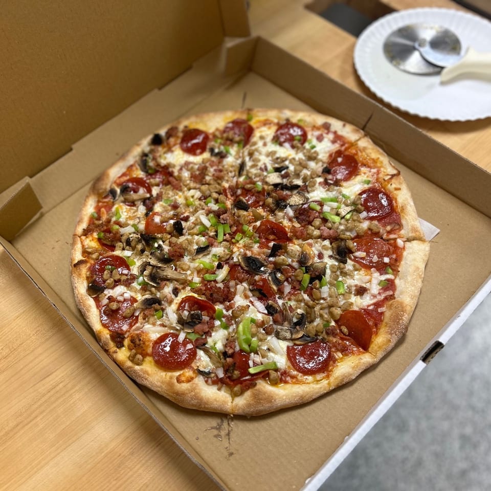 A Jonuzi's Pizza with pepperoni, sausage, mushrooms, onions, and green peppers in a box.