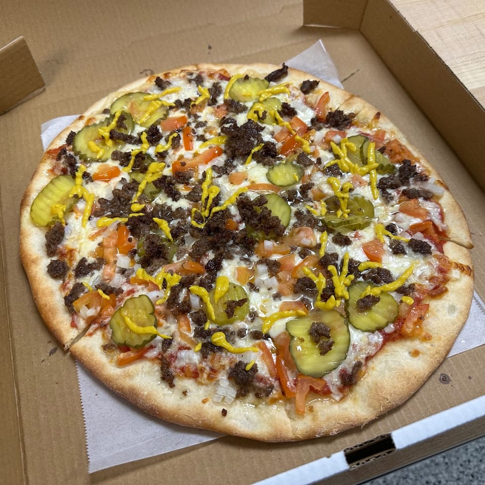 Jonuzi's cheeseburger pizza with ground beef, pickles, tomatoes, onions, and mustard drizzle in a box.